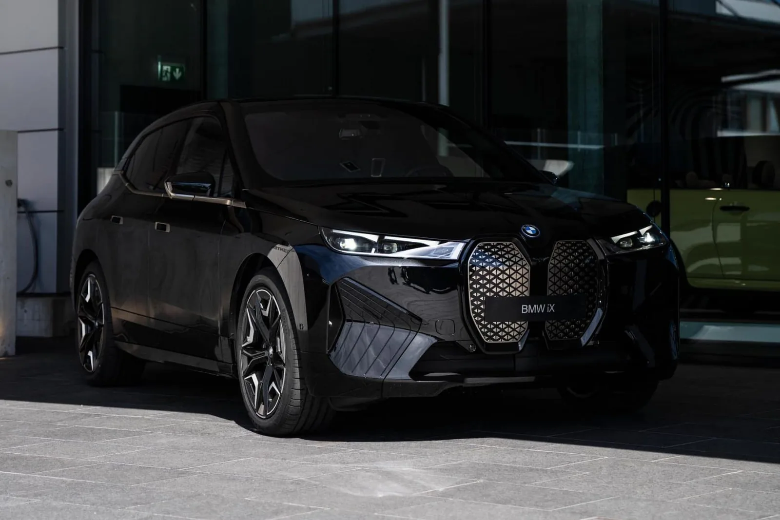 BMW iX xDrive50 in Black Sapphire Metallic, three-quarter front view at a glass-fronted building