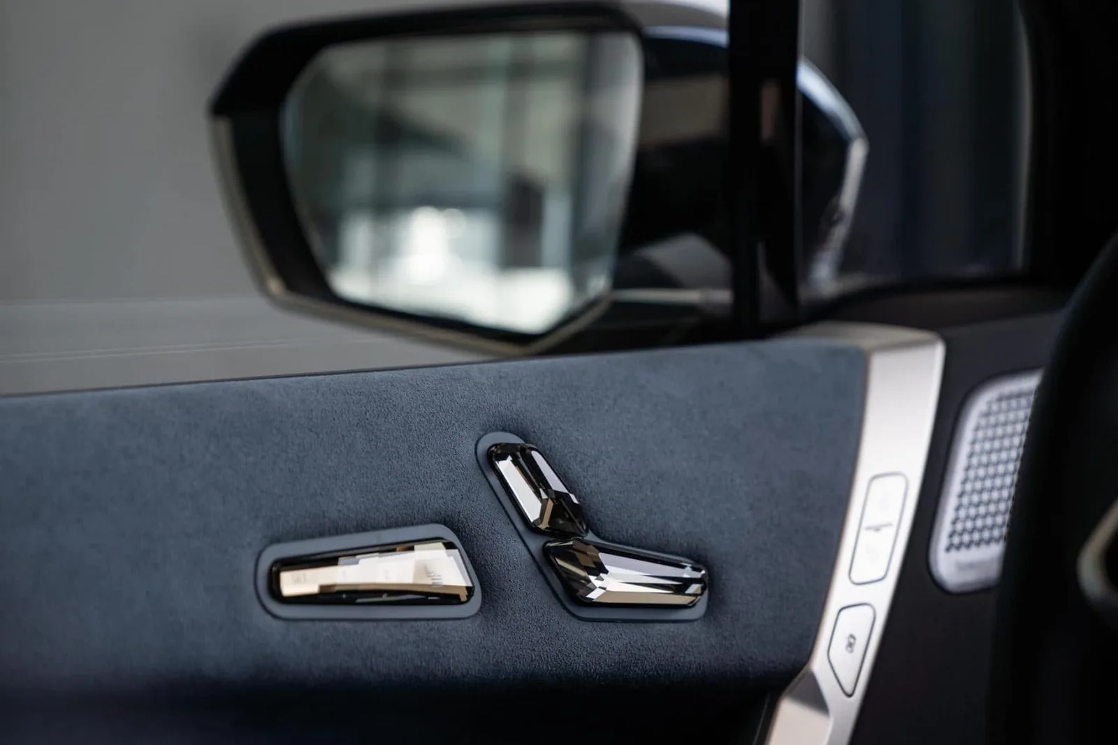 BMW iX door card in suede with glass seat controls and the wing mirror beyond